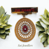 Golden OM SHANTI badge with circular designer locket featuring red stone and diamond-like accents, displayed with green succulents – Sai Jewellers.