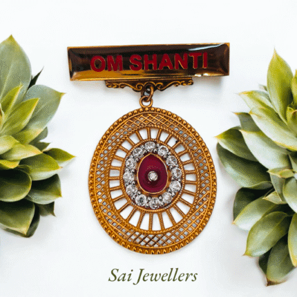 Golden OM SHANTI badge with circular designer locket featuring red stone and diamond-like accents, displayed with green succulents – Sai Jewellers.
